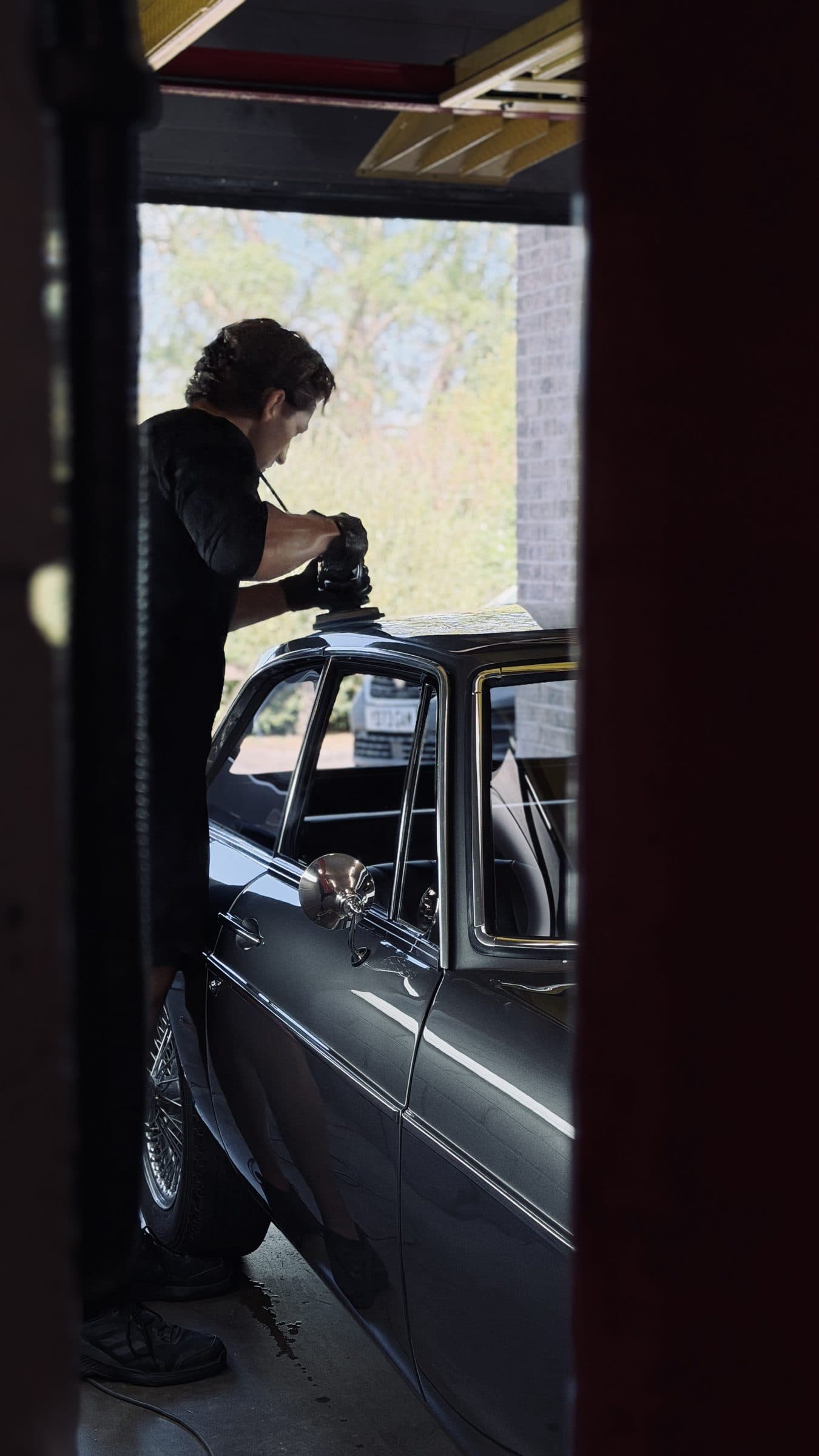 Detailer polishing a grey classic car in the studio doorway