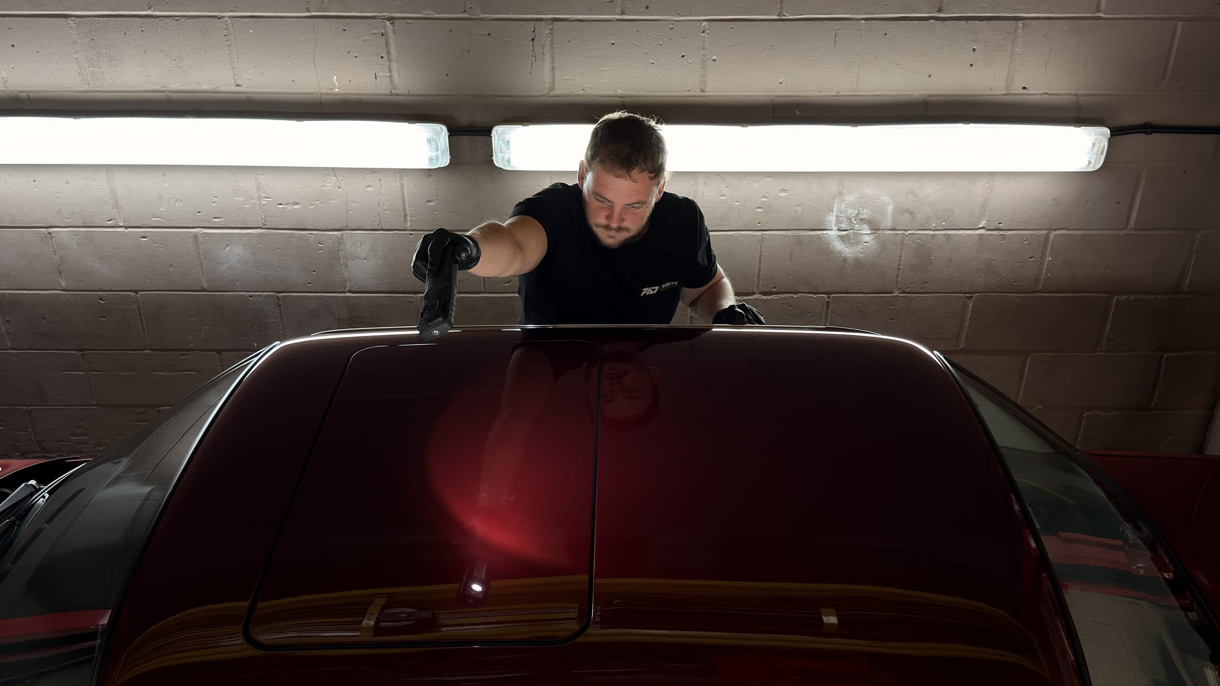 Detailer checking the roof of a dark red car with an inspection light
