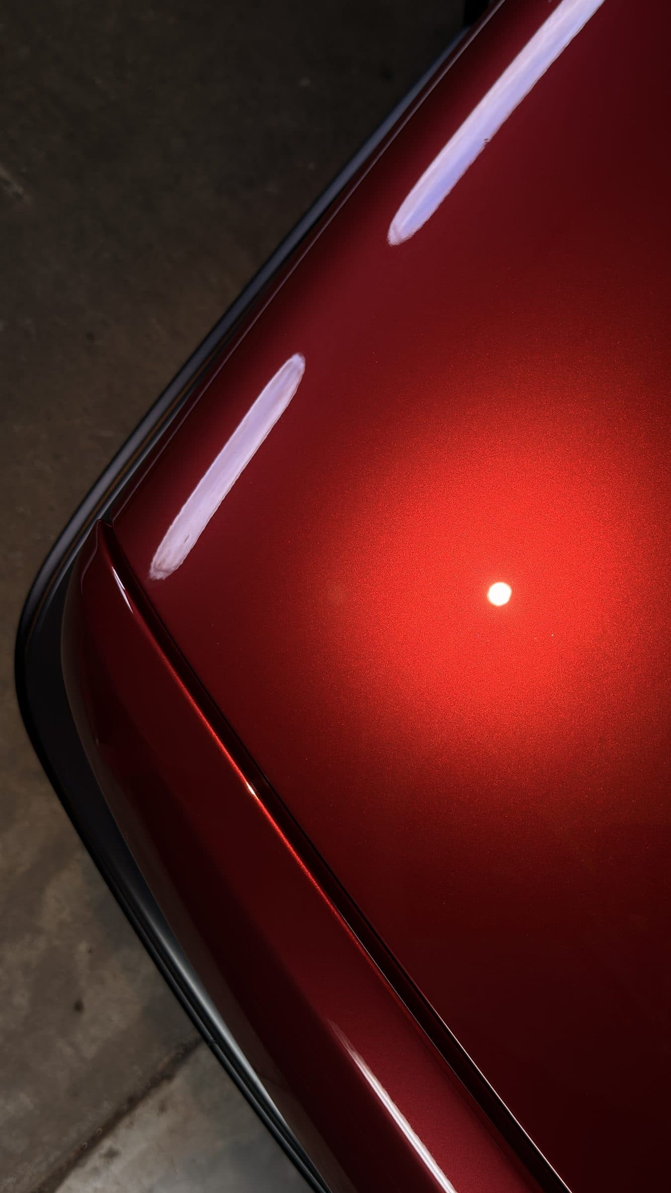 Inspection light and strip-light reflections on dark red metallic paint beside a panel gap